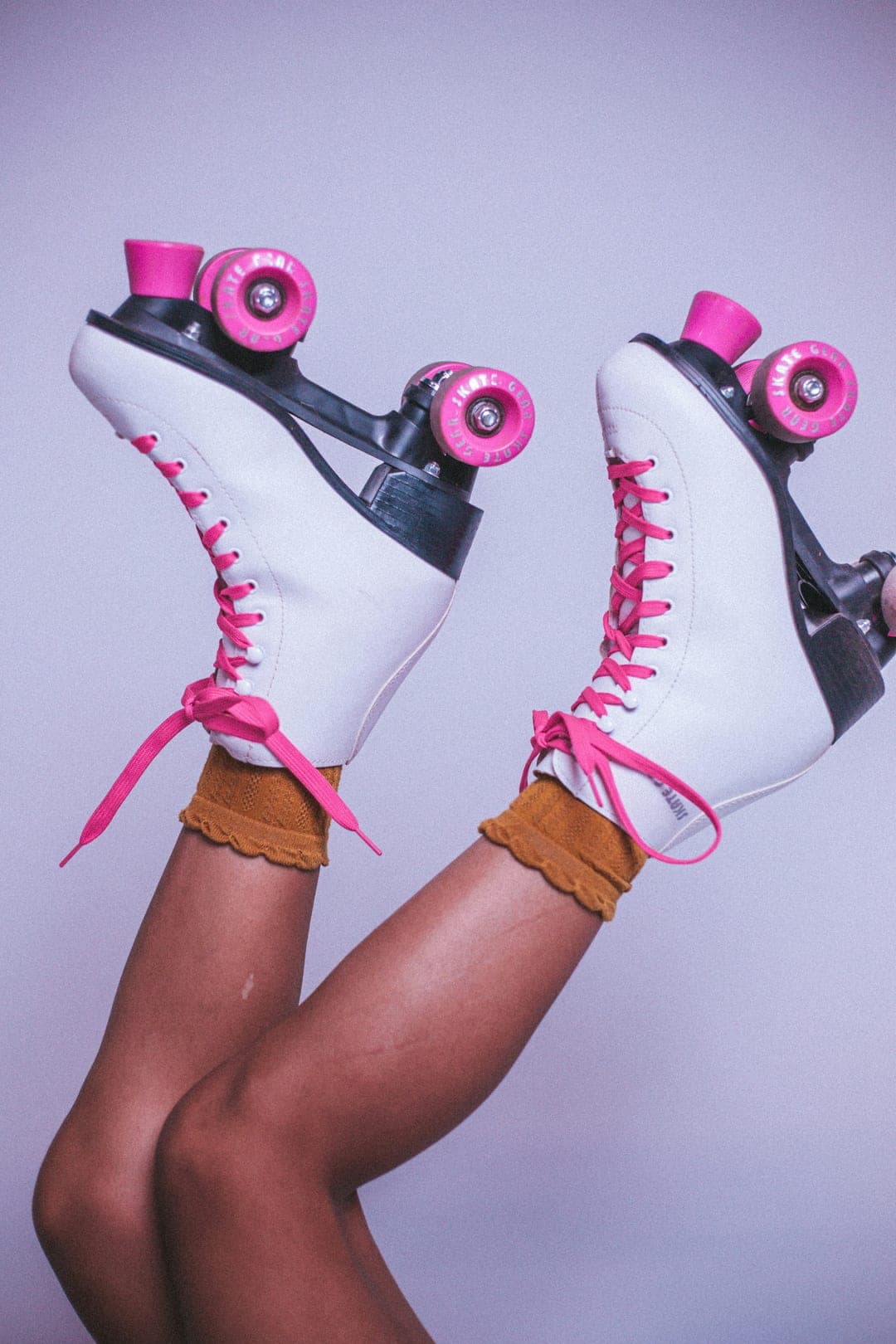 Smooth legs kicked up in white roller skates with hot pink laces