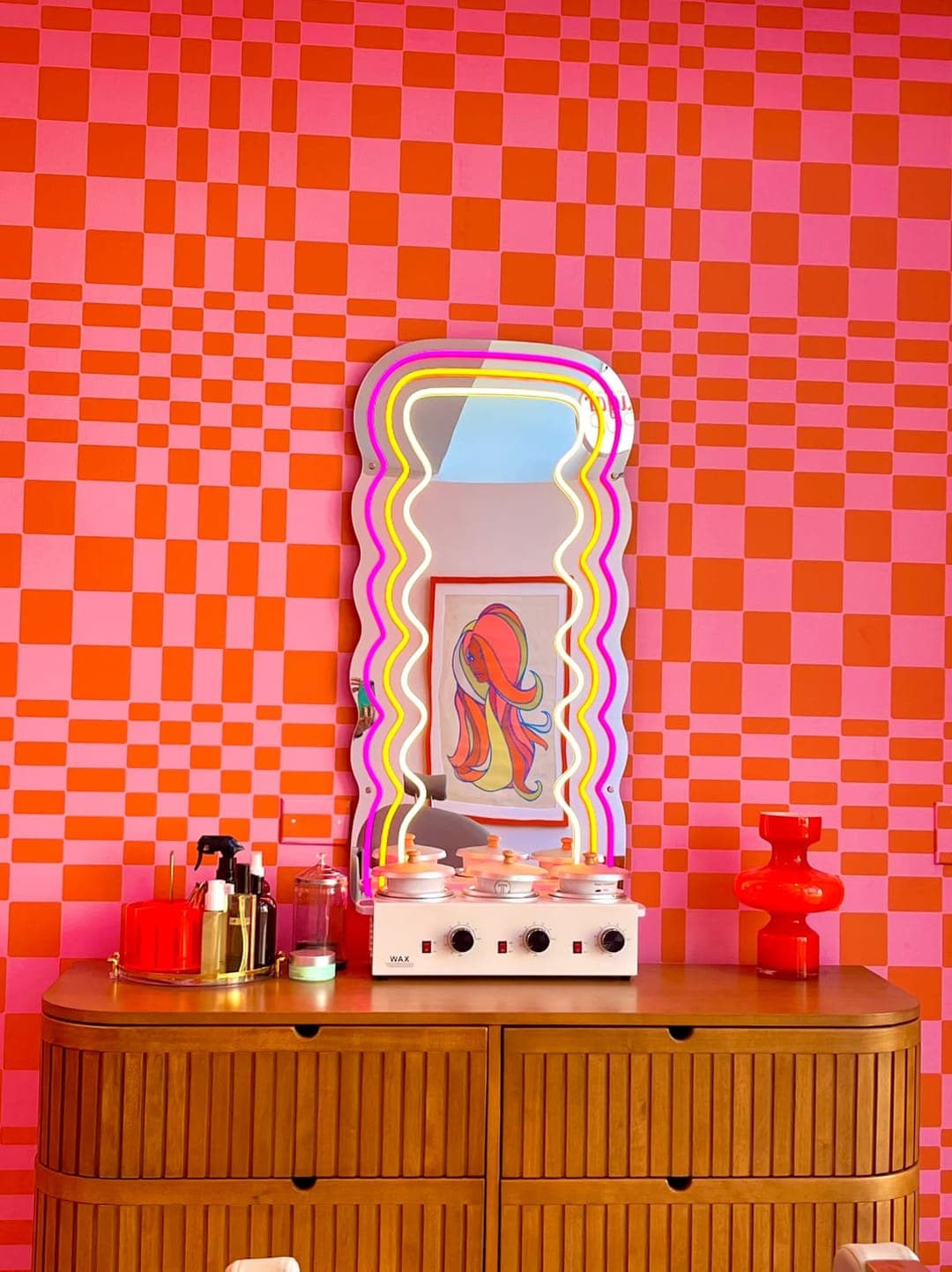 Aftercare products on a wooden dresser under a neon-framed mirror